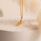The Davina Letter Necklace features a gold pendant shaped like the letter A, elegantly displayed on a textured neutral background—making it an ideal romantic gift.