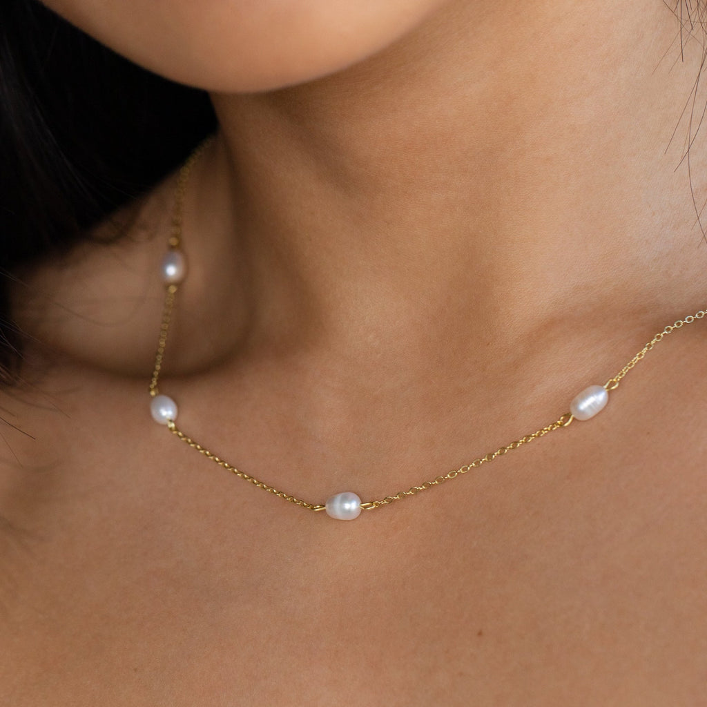 The Anna Pearl Station Necklace features evenly spaced white pearls on a gold chain, resting elegantly on the neck—perfect as a Mother’s Day or bridesmaid gift, shown close up against the skin.