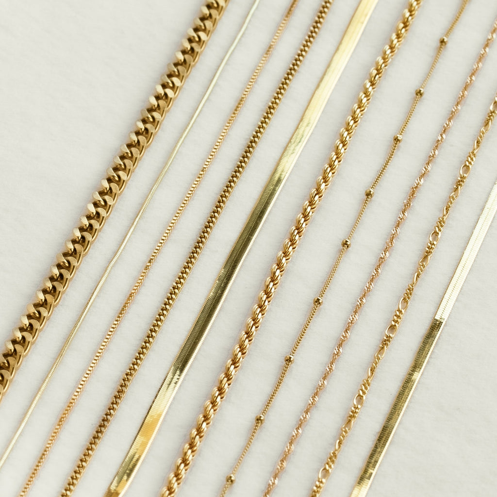 An assortment of gold necklace chains displayed side-by-side on a light surface, showing a range of textures and link styles.