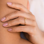 A hand with light pink nails wears the dainty Elora Baguette Wrap Ring, featuring small diamond crystal baguettes, resting on a bare arm.