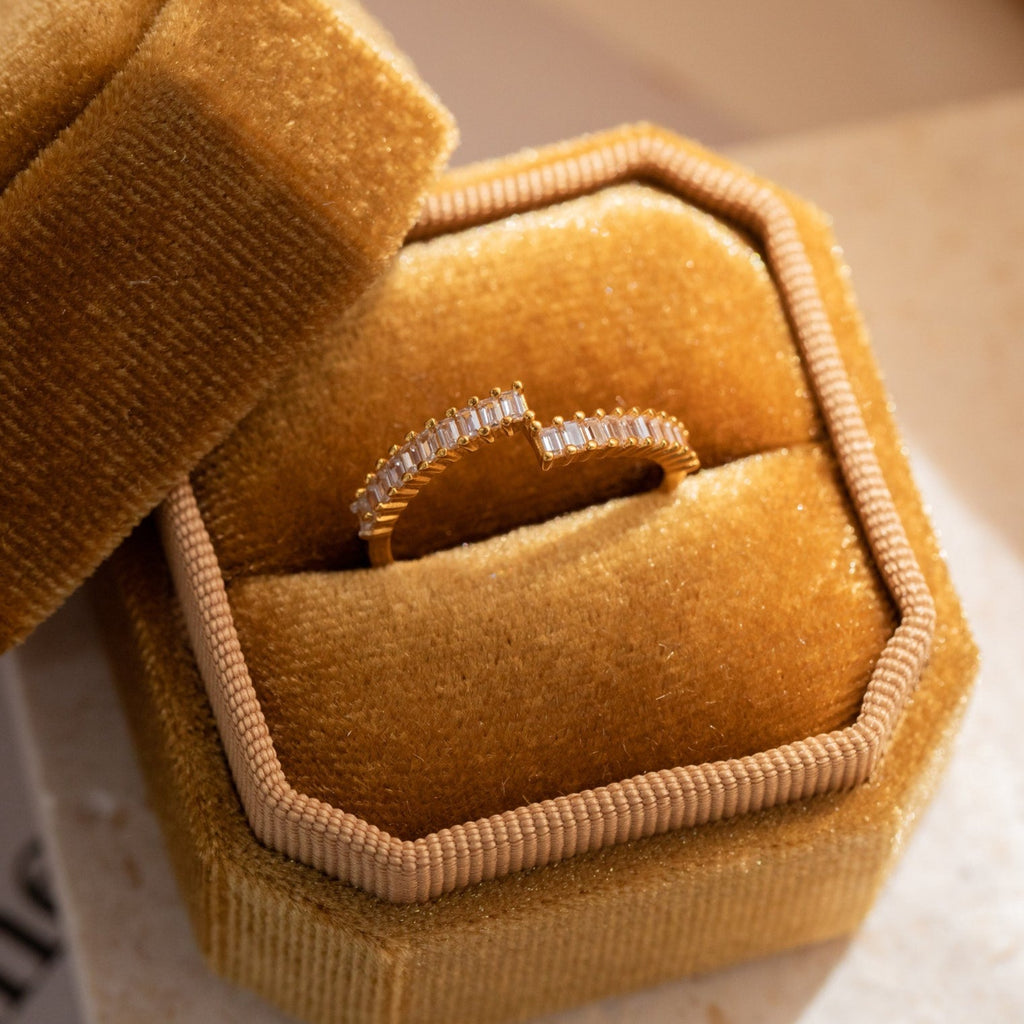 A dainty Elora Baguette Wrap Ring with small diamond baguettes is displayed in a plush, hexagonal gold velvet box, perfectly capturing the ring’s elegance.