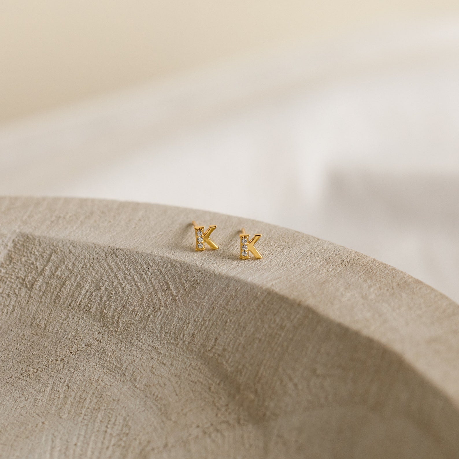 Pave Initial Studs—gold and diamond letter K earrings set on a textured, light-colored surface—make a perfect personalized gift.