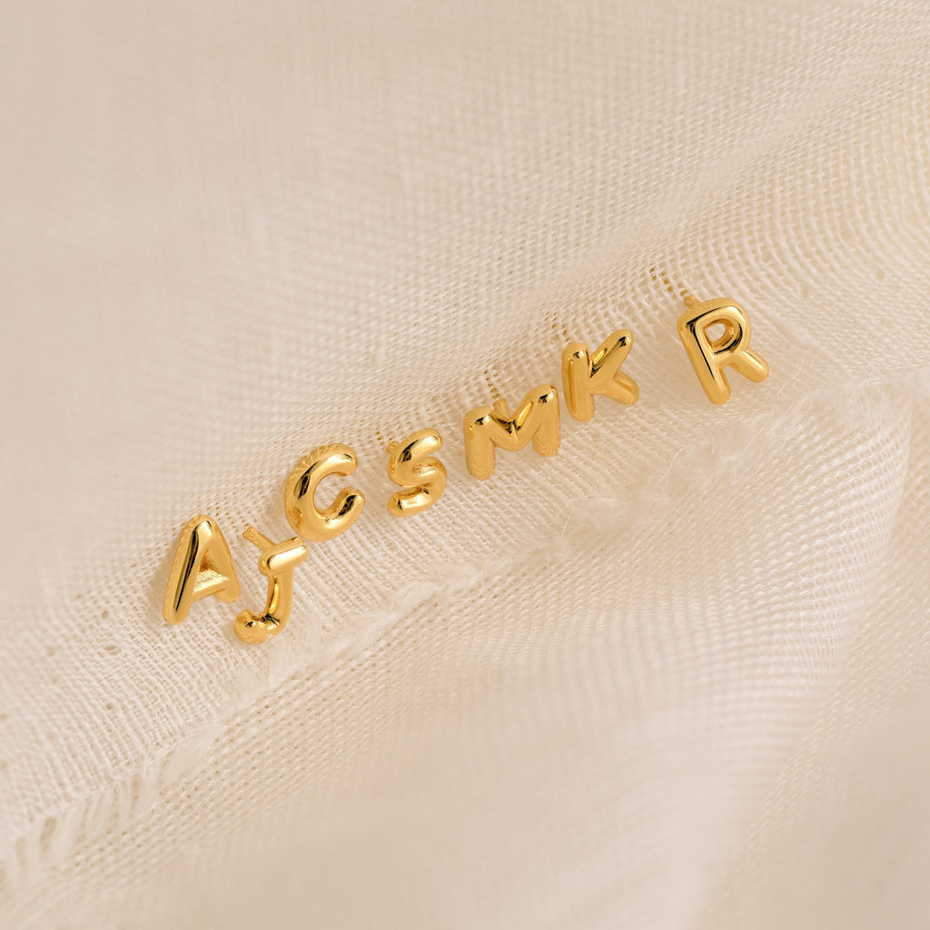 Bubble Letter Studs in gold—choose from letters A, J, C, S, M, K, or R. Displayed on a light textured fabric; they’re ideal for customizing earrings or gifting to bridesmaids.