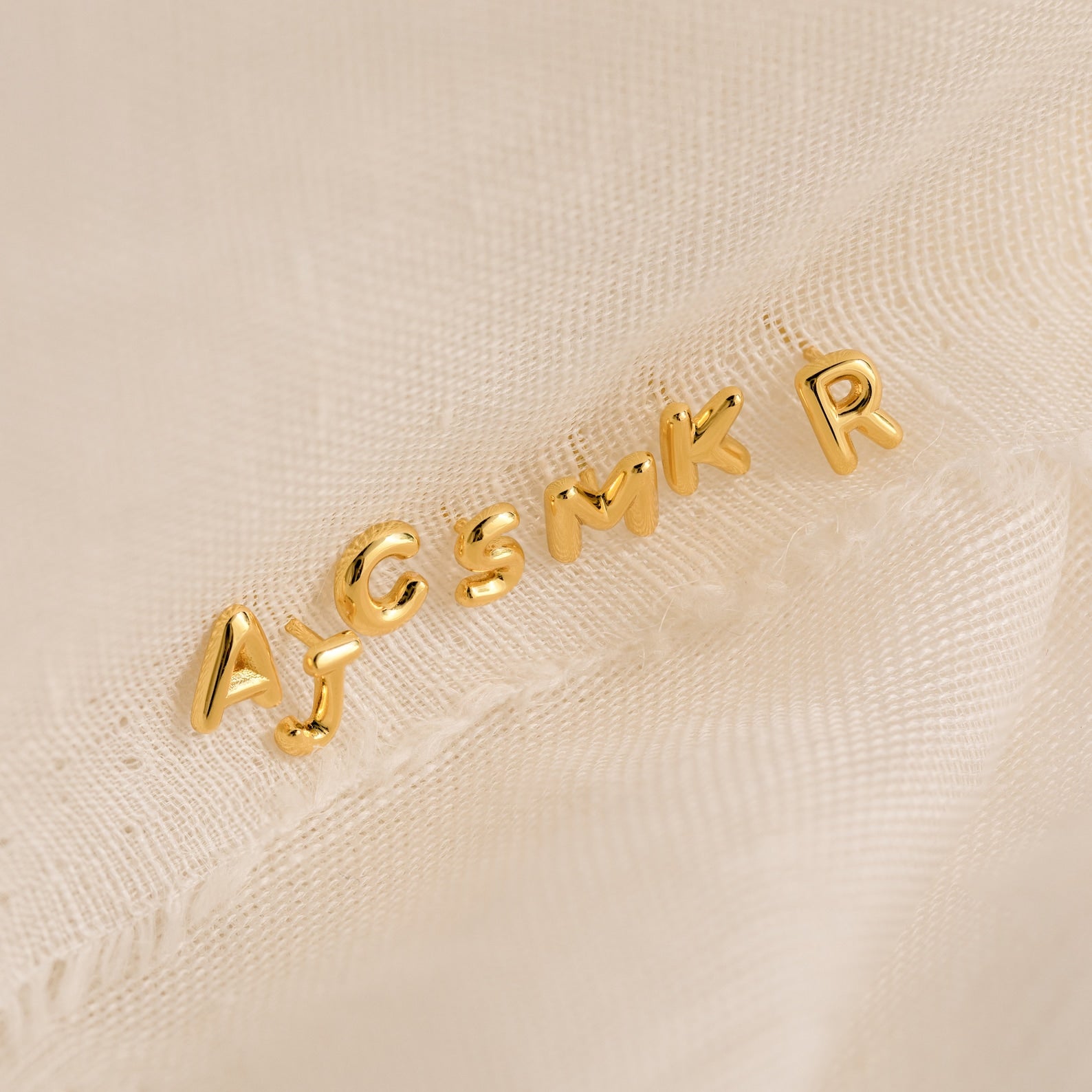 Bubble Letter Studs in gold—choose from letters A, J, C, S, M, K, or R. Displayed on a light textured fabric; they’re ideal for customizing earrings or gifting to bridesmaids.