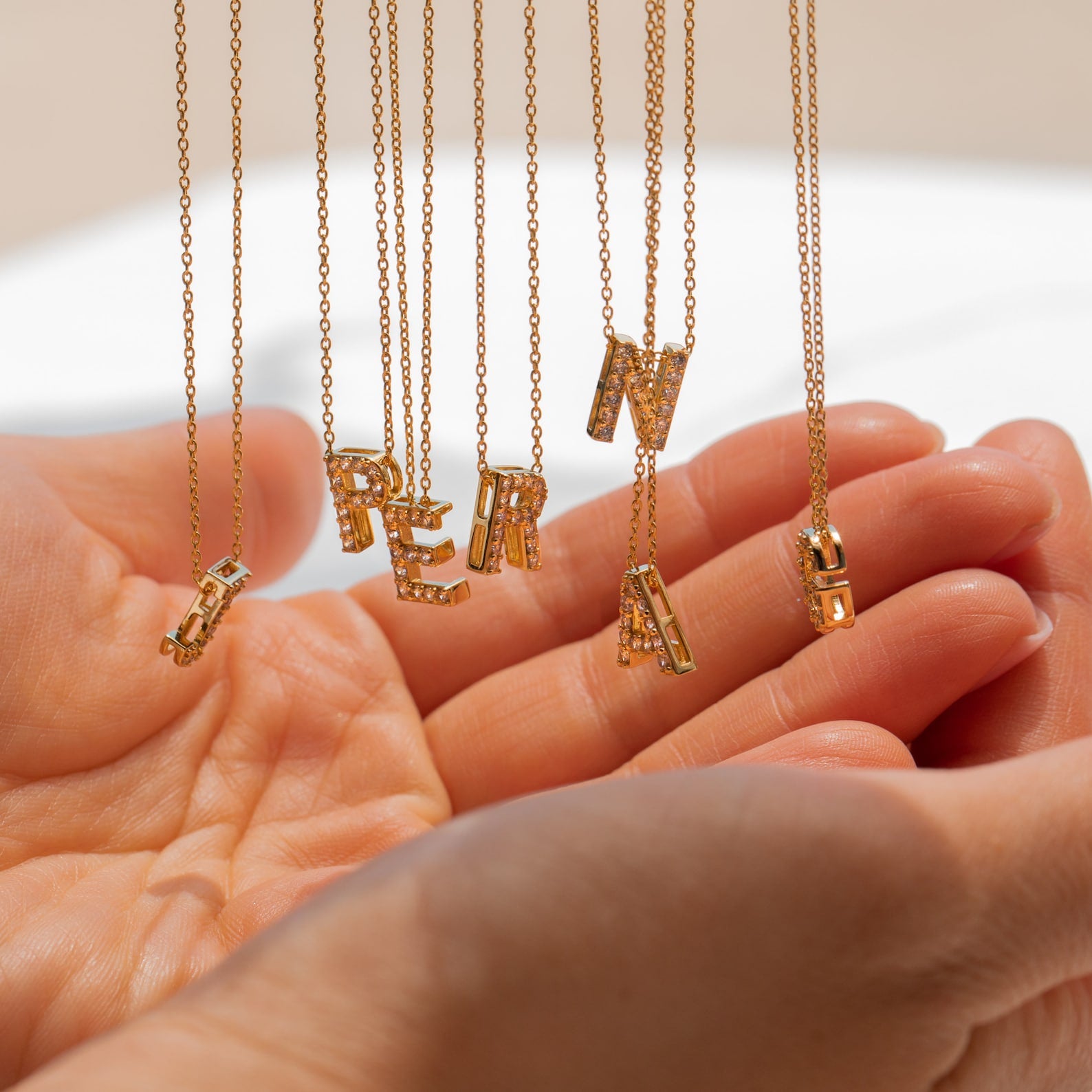 Floating Pave Initial Necklaces spelling S-E-R-A-P-N-A rest in open hands—a stunning, personalized jewelry piece that sparkles with every initial.