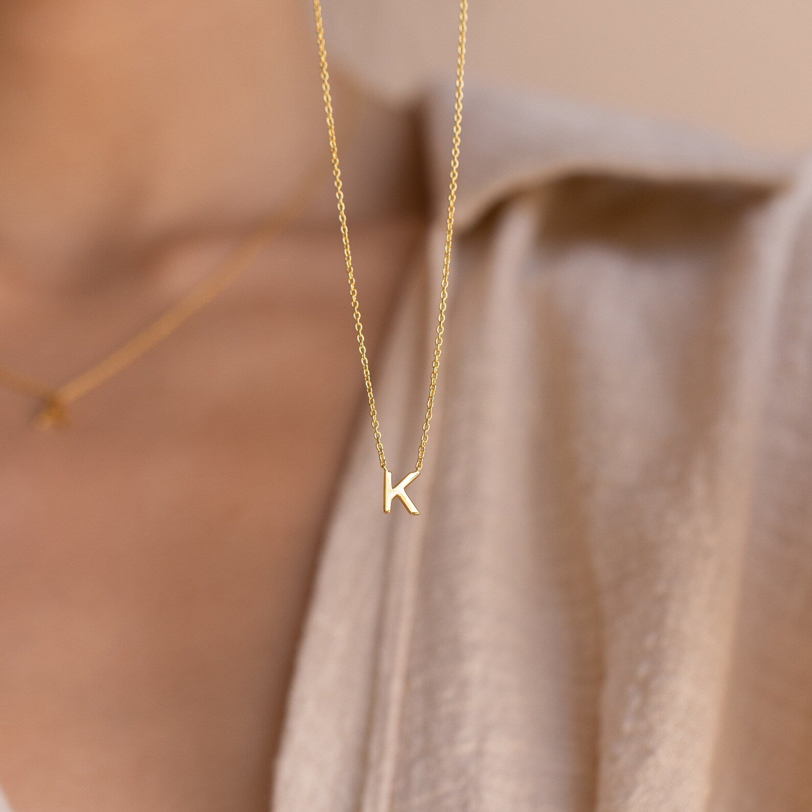 Dainty Initial Necklace featuring a gold letter K pendant, styled over a beige shirt with a blurred background—an ideal customizable accessory and thoughtful Christmas gift.