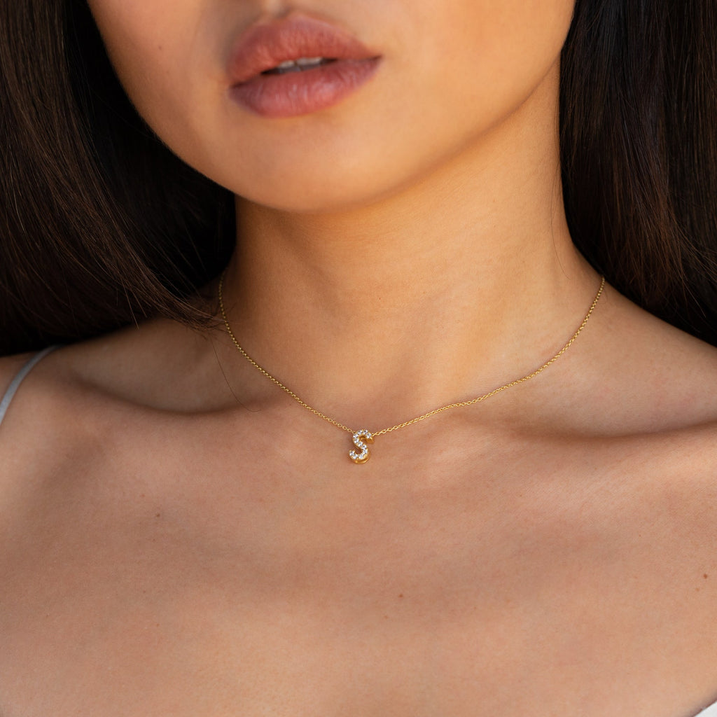 A woman wears the Floating Pave Initial Necklace featuring a small, sparkling S pendant—a beautiful piece of personalized jewelry.