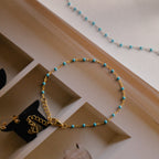 The Turquoise Station Bracelet features a gold chain with small turquoise beads, adding a boho touch to your bracelet stack. Shown styled on an open book.