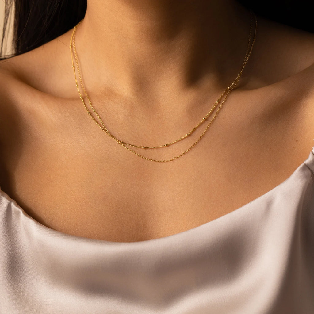 Woman wearing a white satin top styled with the Beaded Duo Chain Necklace—a set of two layered gold necklaces, including a minimalist choker that beautifully complements her look.