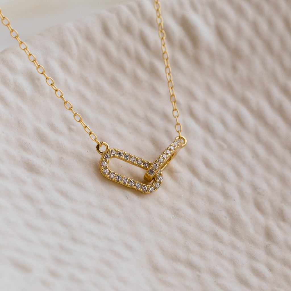 The Pave Linked Pendant Necklace features two interlocking, diamond-studded oval links on a gold chain—ideal for adding a touch of glamour to any outfit.