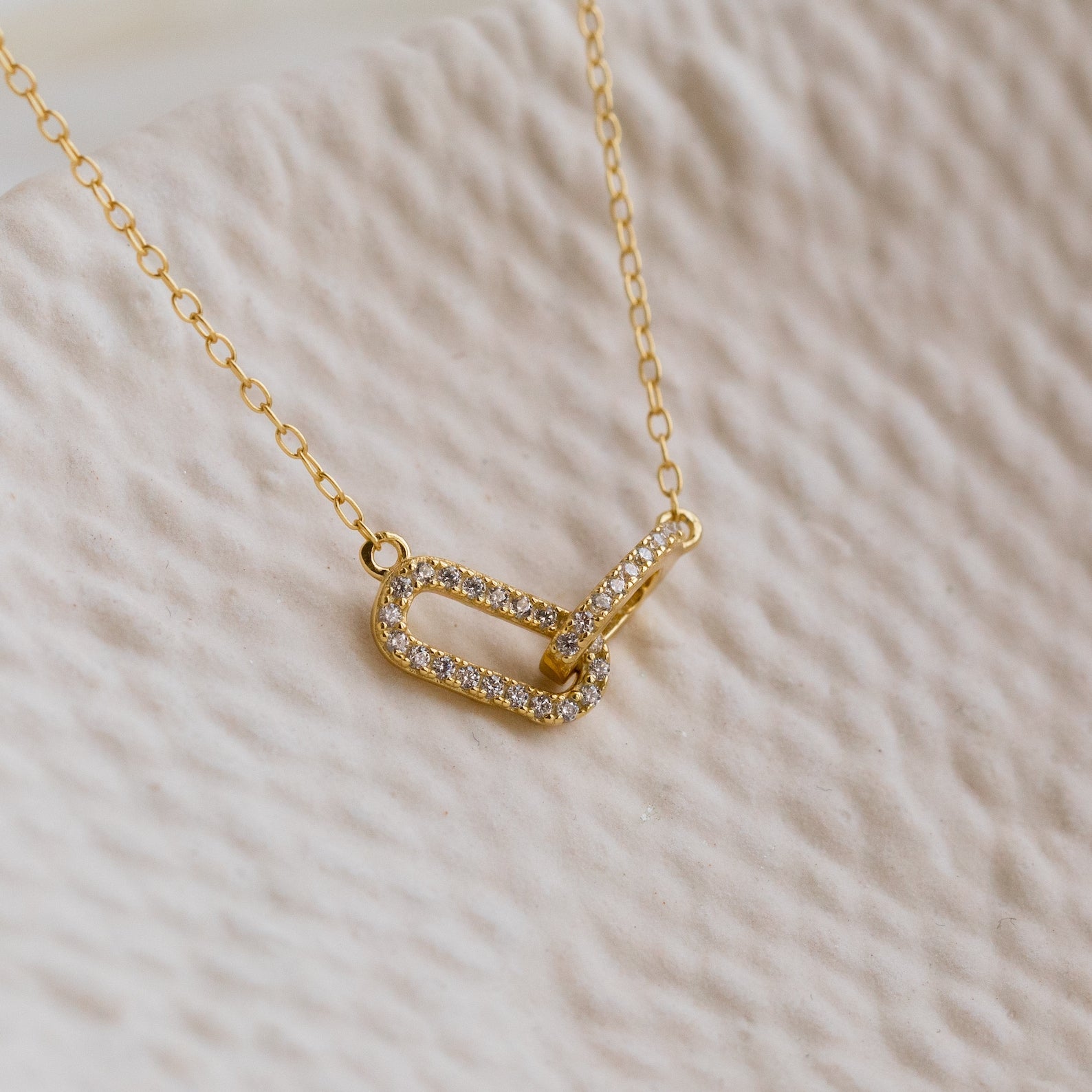 The Pave Linked Pendant Necklace features two interlocking, diamond-studded oval links on a gold chain—ideal for adding a touch of glamour to any outfit.