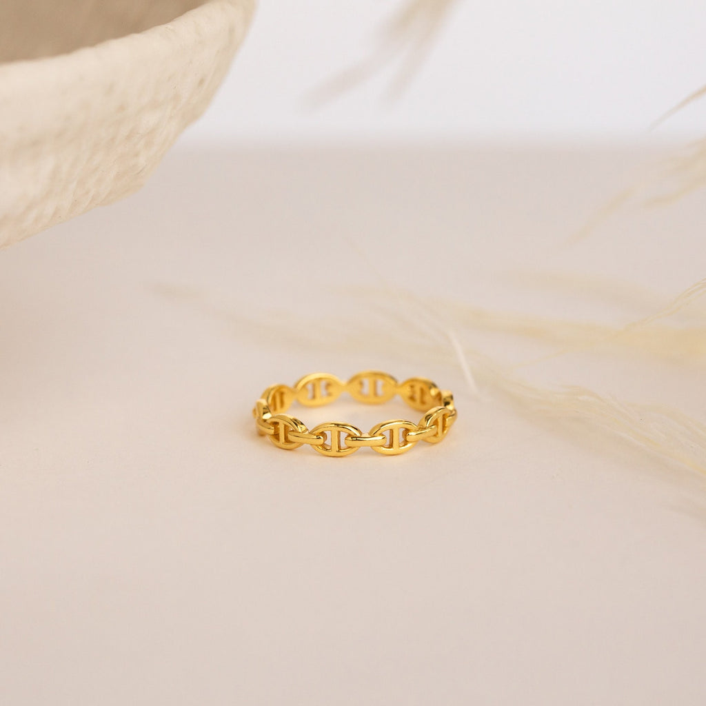 The Reese Link Ring, a minimalist gold chain ring, features elegant link details displayed on a light beige surface with a soft, neutral background.
