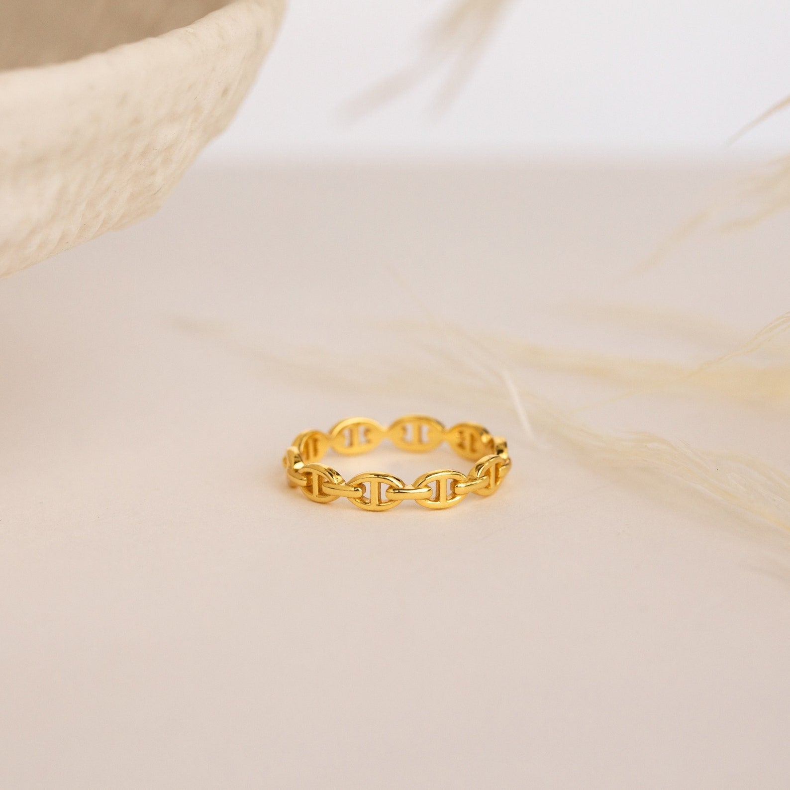 The Reese Link Ring, a minimalist gold chain ring, features elegant link details displayed on a light beige surface with a soft, neutral background.