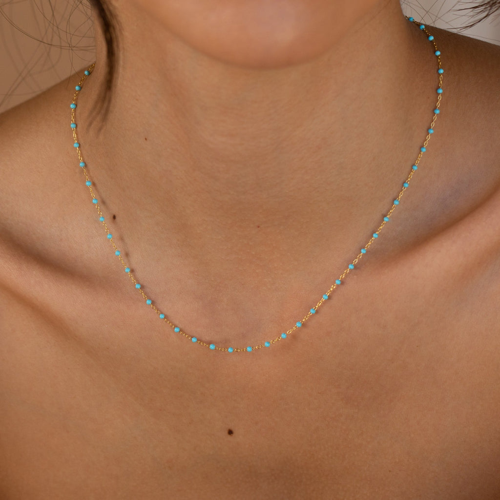 The Turquoise Station Necklace features a delicate gold chain adorned with small turquoise beads, resting gracefully on the neck and collarbone.