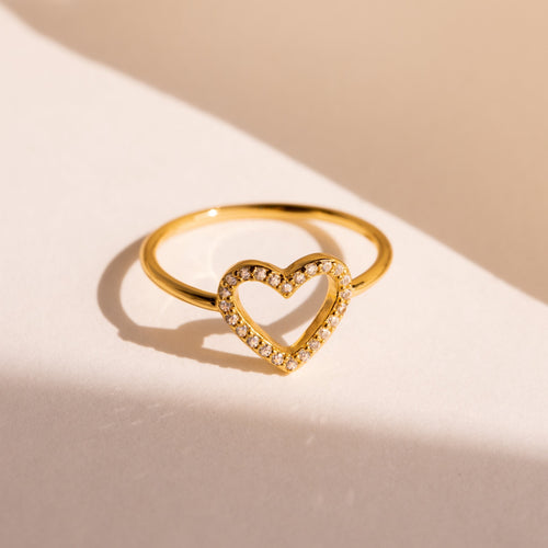 The Aphrodite Pave Heart Ring features an open heart outline paved with sparkling diamonds, shown on a cream-colored background—an ideal anniversary gift.