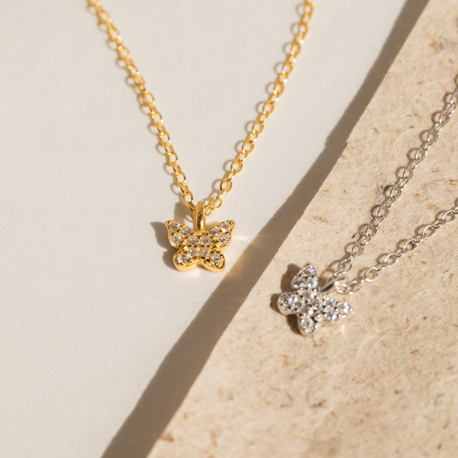 The Mandy Pave Butterfly Necklace, adorned with diamond gemstones, is beautifully displayed on textured beige and cream surfaces.