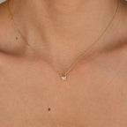 Gold chain necklace with a small butterfly-shaped pendant adorned with clear gemstones, worn with a strapless nude top.