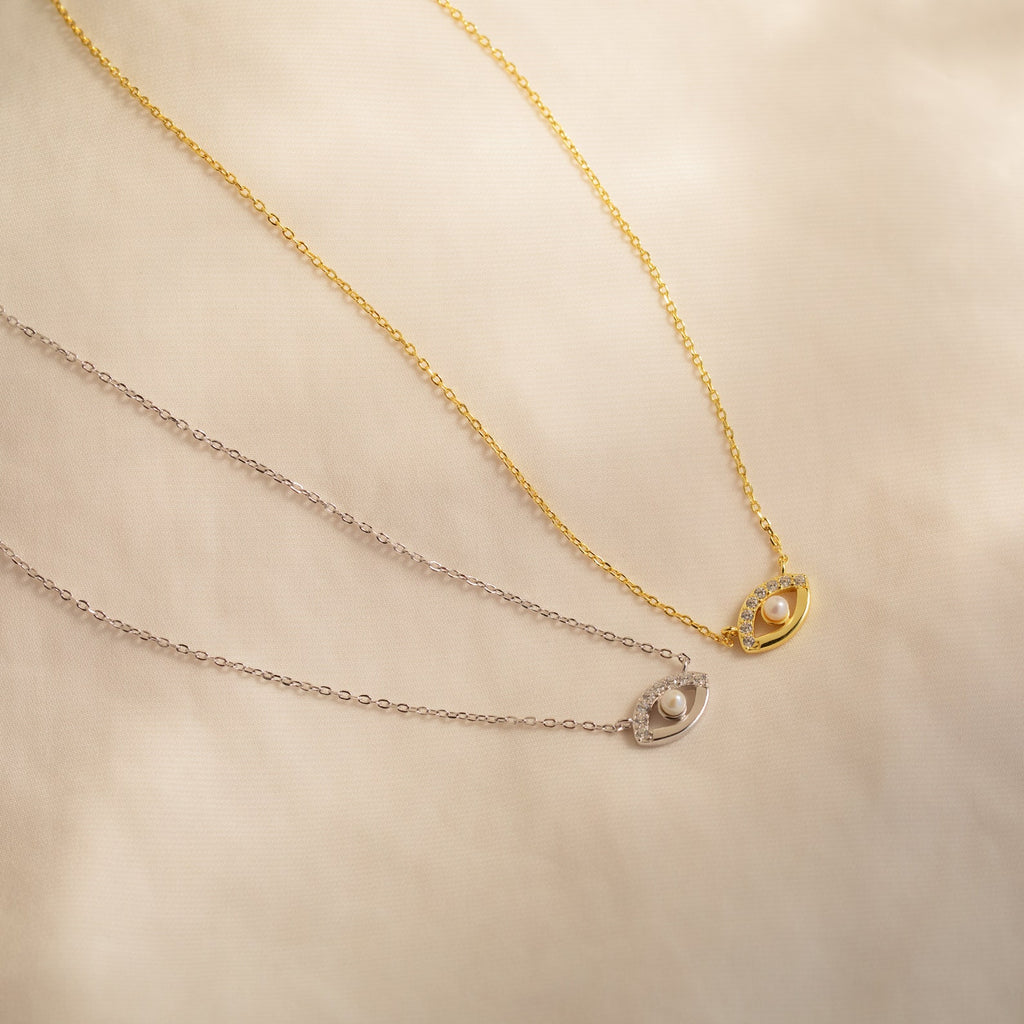 Two delicate Amaryllis Pave Evil Eye Necklaces, one gold and one silver, each featuring an oval pendant with a small pearl bead for added protection.