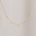The Marquise Station Necklace features a delicate chain with small marquise-shaped diamond charms, displayed against a light fabric background.