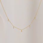 The Marquise Station Necklace features a delicate chain with small marquise-shaped diamond charms, displayed against a light fabric background.