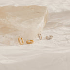 The Clarissa Pave Huggies—one gold pair and one silver—are small hoop earrings displayed on a textured white surface, ideal for date nights or elevating your everyday style.