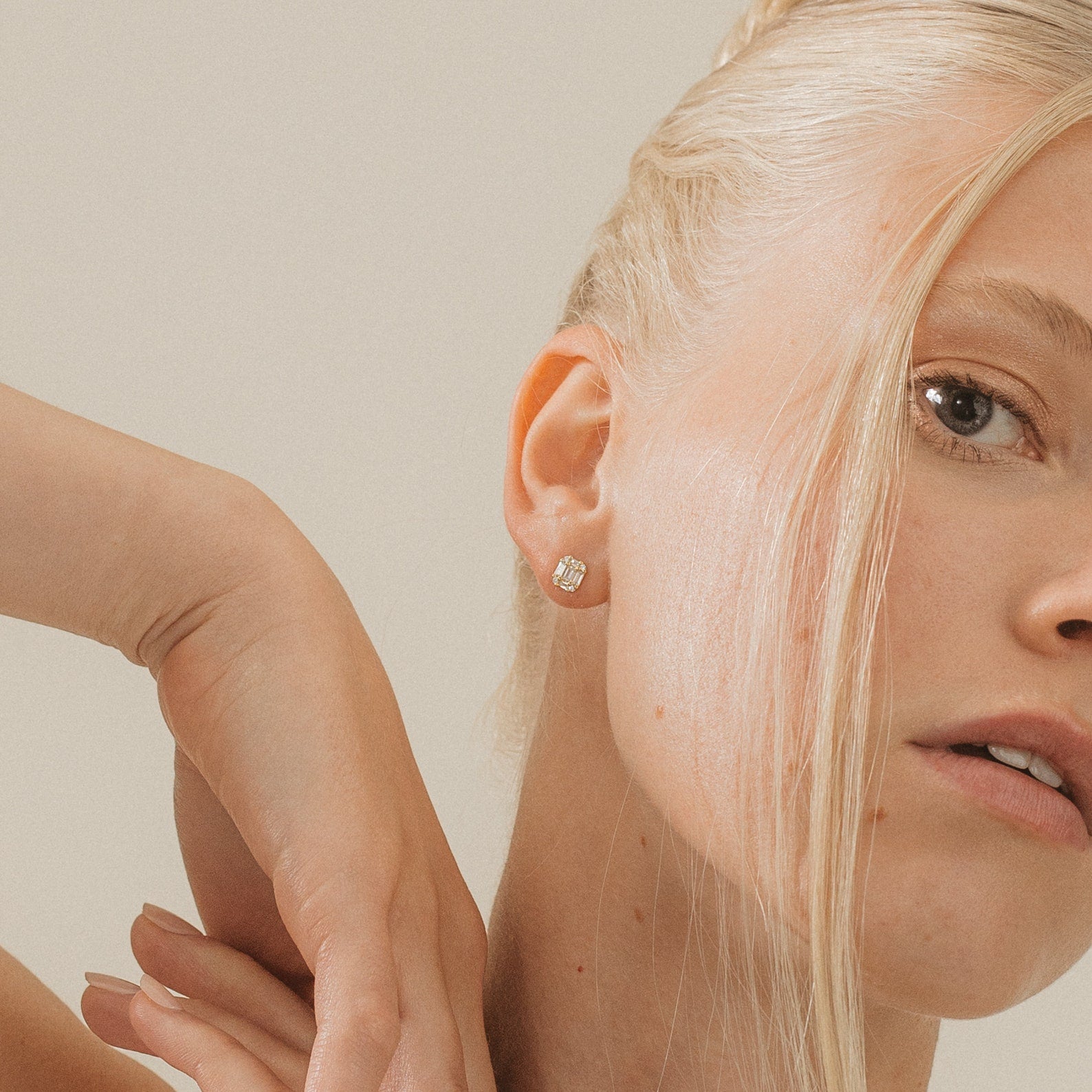 Close-up of a blonde woman wearing Arabella Diamond Studs, posing with her hand near her face.