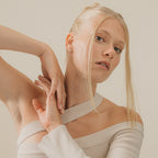 A blonde woman in a cream off-shoulder top poses with arms raised against a neutral background, showcasing the elegant Arabella Diamond Studs.