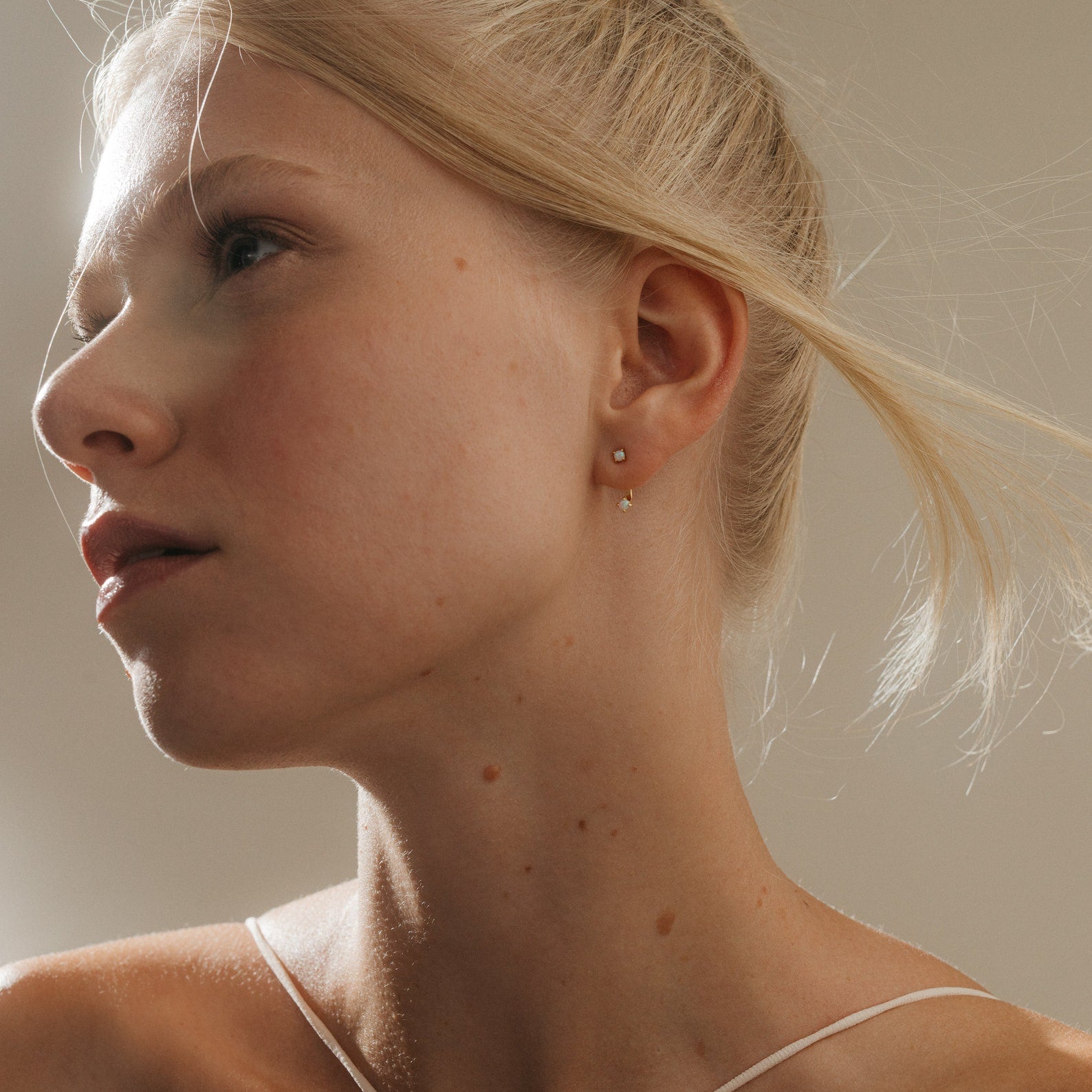 A blonde-haired woman in a bun looks to the side, wearing a thin strap top and minimalist Opal Ear Jackets.