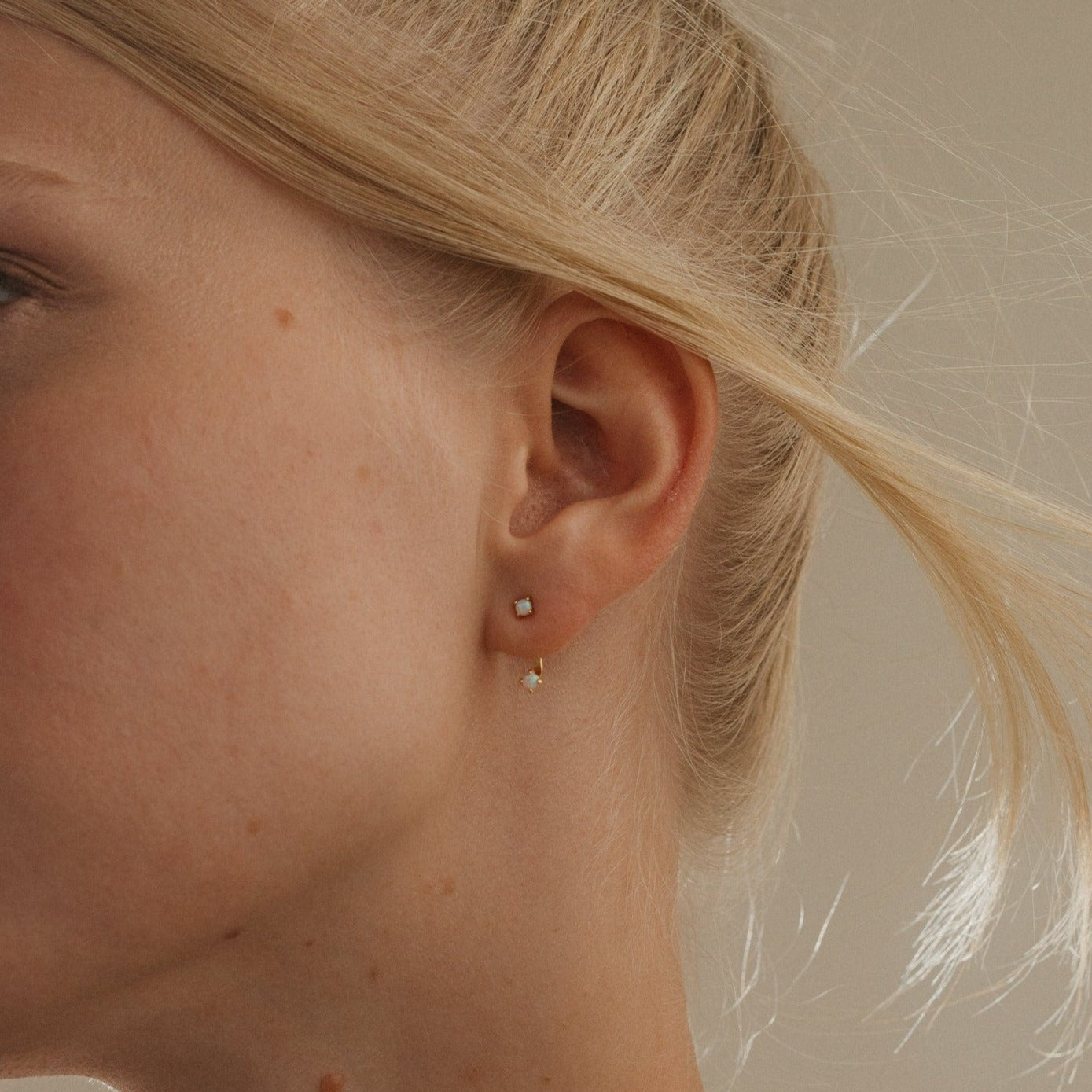 Close-up of a woman's ear with her blonde hair pulled back, showcasing the minimalist Opal Ear Jackets in gold.