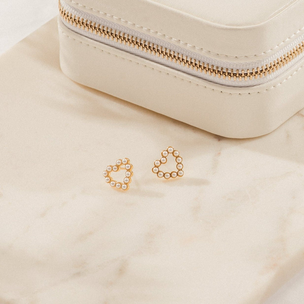 Pearl Heart Studs featuring gold heart-shaped designs with dainty beaded charms are displayed next to a cream jewelry box on a beige marble surface, ideal for vintage jewelry enthusiasts.