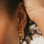 Close-up of an ear adorned with Jocelyn Diamond Studs and a gold twisted hoop—hand gently touching hair. These dainty, sparkling studs are perfect everyday earrings for a subtle, elegant look.