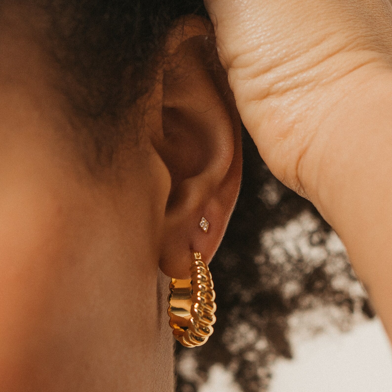 Close-up of an ear adorned with Jocelyn Diamond Studs and a gold twisted hoop—hand gently touching hair. These dainty, sparkling studs are perfect everyday earrings for a subtle, elegant look.