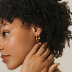 Woman with curly hair touches her ear, wearing Jocelyn Diamond Studs and looking to the left.