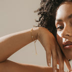 A woman with curly hair rests her hand on her face, wearing the Venus Diamond Station Bracelet—a delicate piece featuring a small charm, perfect as elegant wedding jewelry or a thoughtful anniversary gift.
