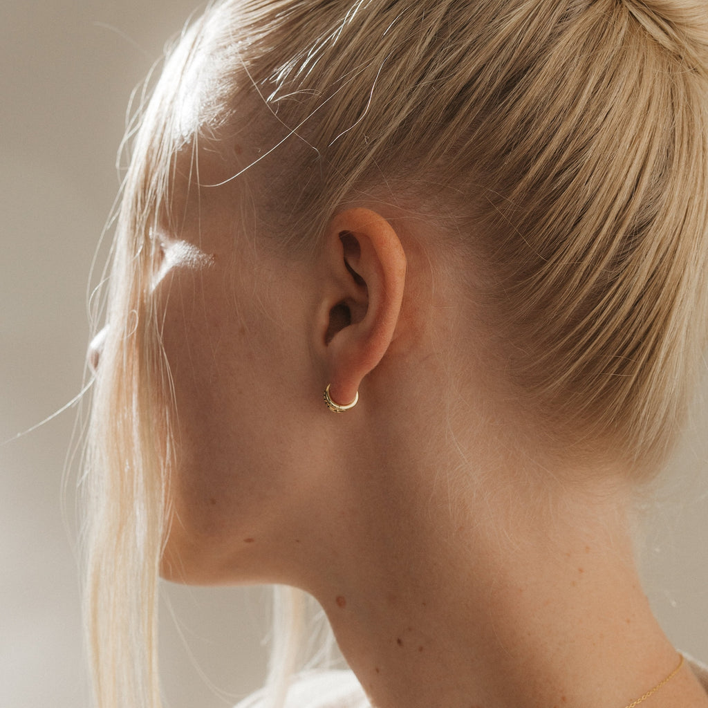 A blonde woman with her hair in a bun is shown in profile, wearing the Amelia Onyx Duo Huggies.
