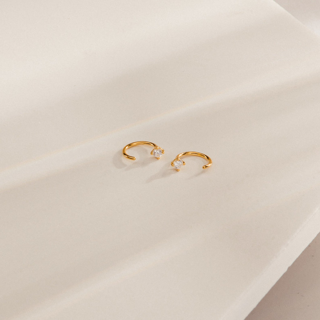 The Saylor III Huggies are dainty diamond hoop earrings resting on a white surface, ideal as petite earrings for everyday elegance.