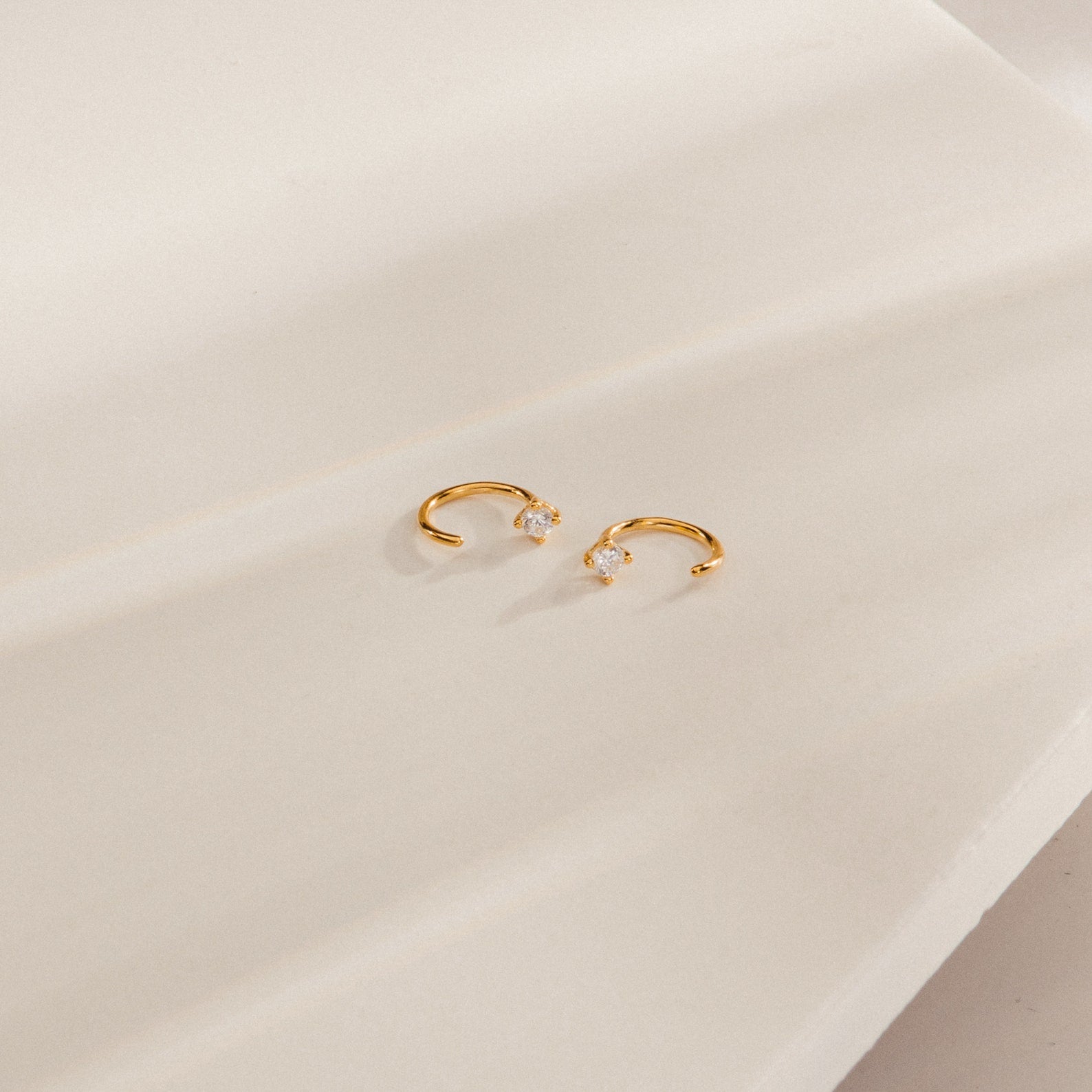 The Saylor III Huggies are dainty diamond hoop earrings resting on a white surface, ideal as petite earrings for everyday elegance.