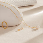 The Ariel Pearl Necklace, paired with a gold ring and pearl earrings, is elegantly displayed on a beige textured surface—ideal for bridal or bridesmaid jewelry.