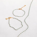 The Turquoise Station Bracelet, a gold chain with small turquoise beads, is shown as part of a bracelet stack alongside a matching necklace on a white background.