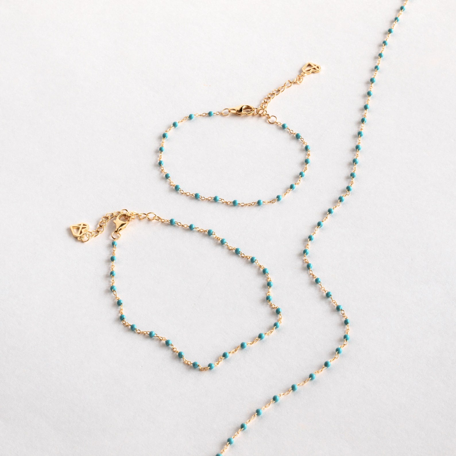 The Turquoise Station Bracelet, a gold chain with small turquoise beads, is shown as part of a bracelet stack alongside a matching necklace on a white background.