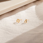 The Lucky Studs Set, featuring a wishbone and a diamond horseshoe stud earring, rests on a softly sunlit fabric surface.