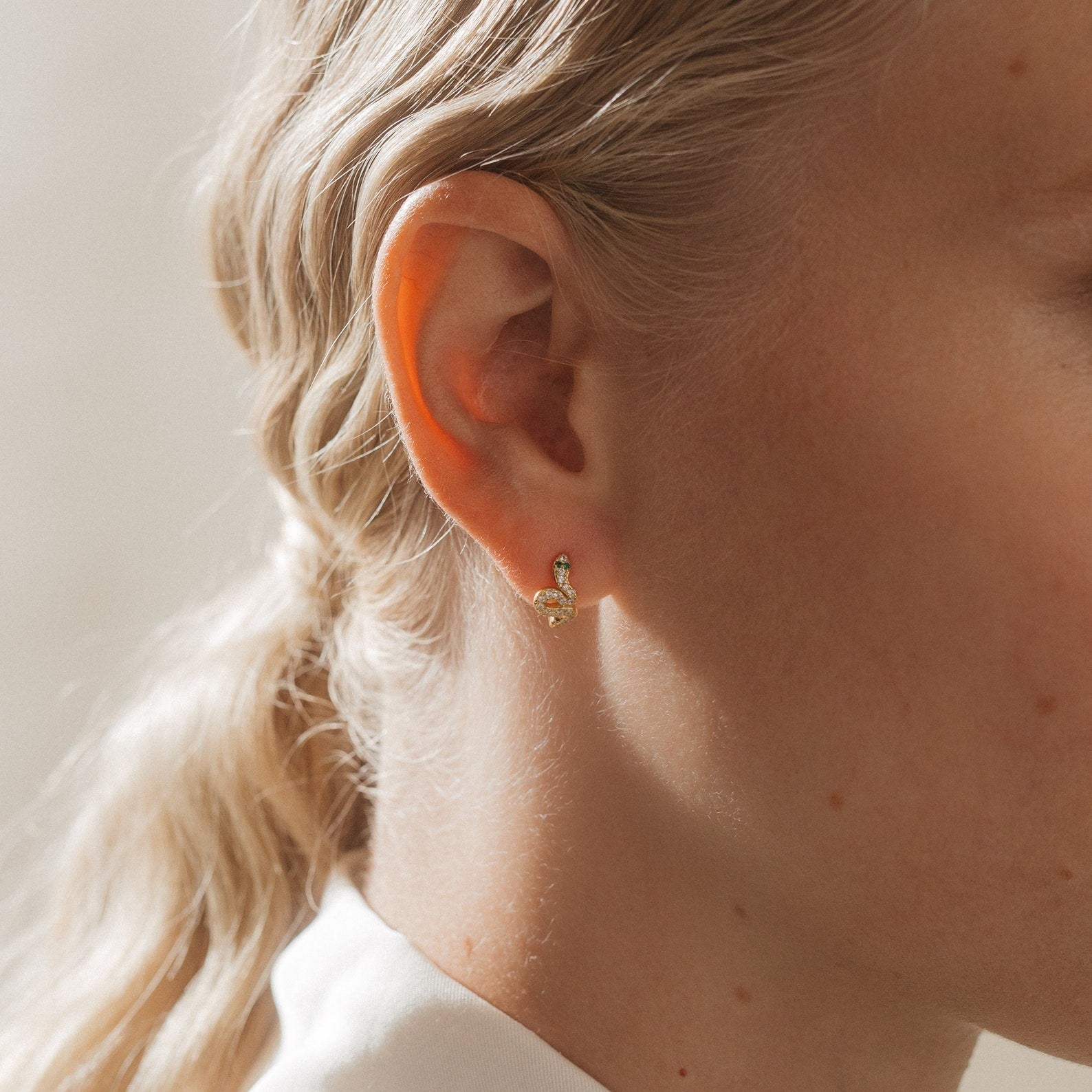 Close-up of a woman's ear wearing Cobra Snake Huggies, showcasing trendy gold earrings with timeless elegance.