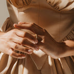 A woman in a satin beige dress showcases the stunning Verity Diamond Ring on her finger, her hands gently touching.