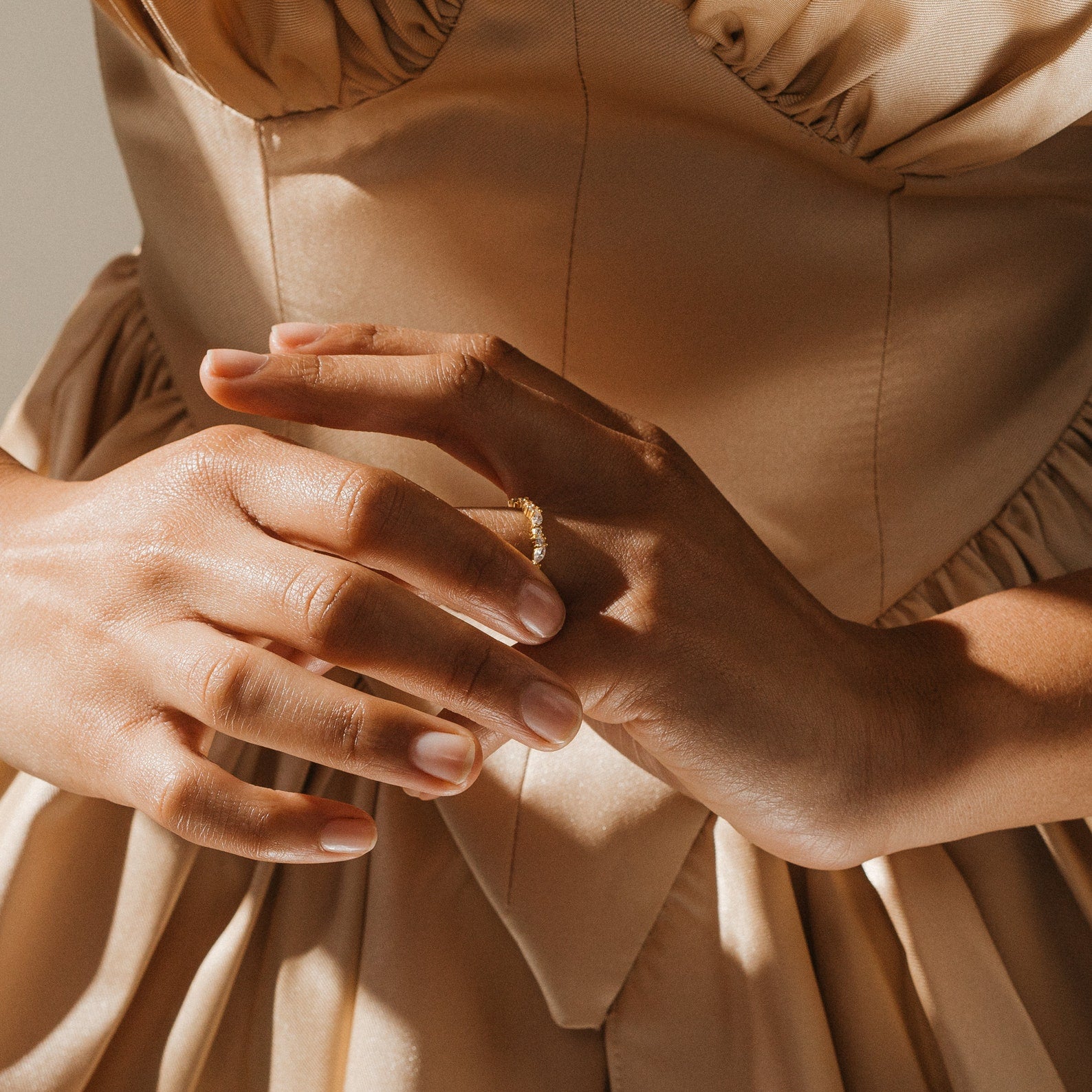 A woman in a satin beige dress showcases the stunning Verity Diamond Ring on her finger, her hands gently touching.