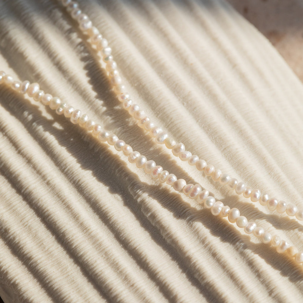 Detail shot of the Brinley Pearl Anklet draped against a neutral textured surface, highlighting the pearls’ smooth, luminous finish and elegant simplicity