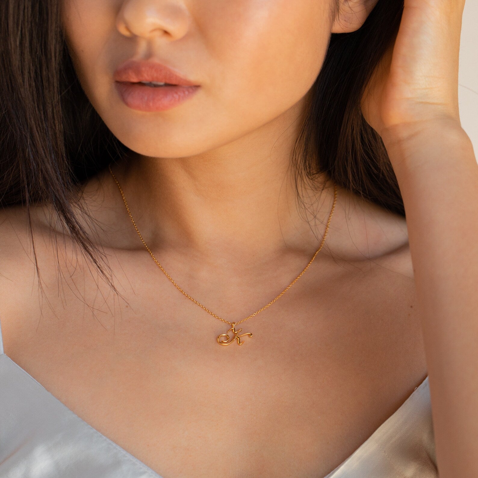 Woman wearing the Davina Letter Necklace and a white top, gently touching her hair—an elegant, romantic gift.