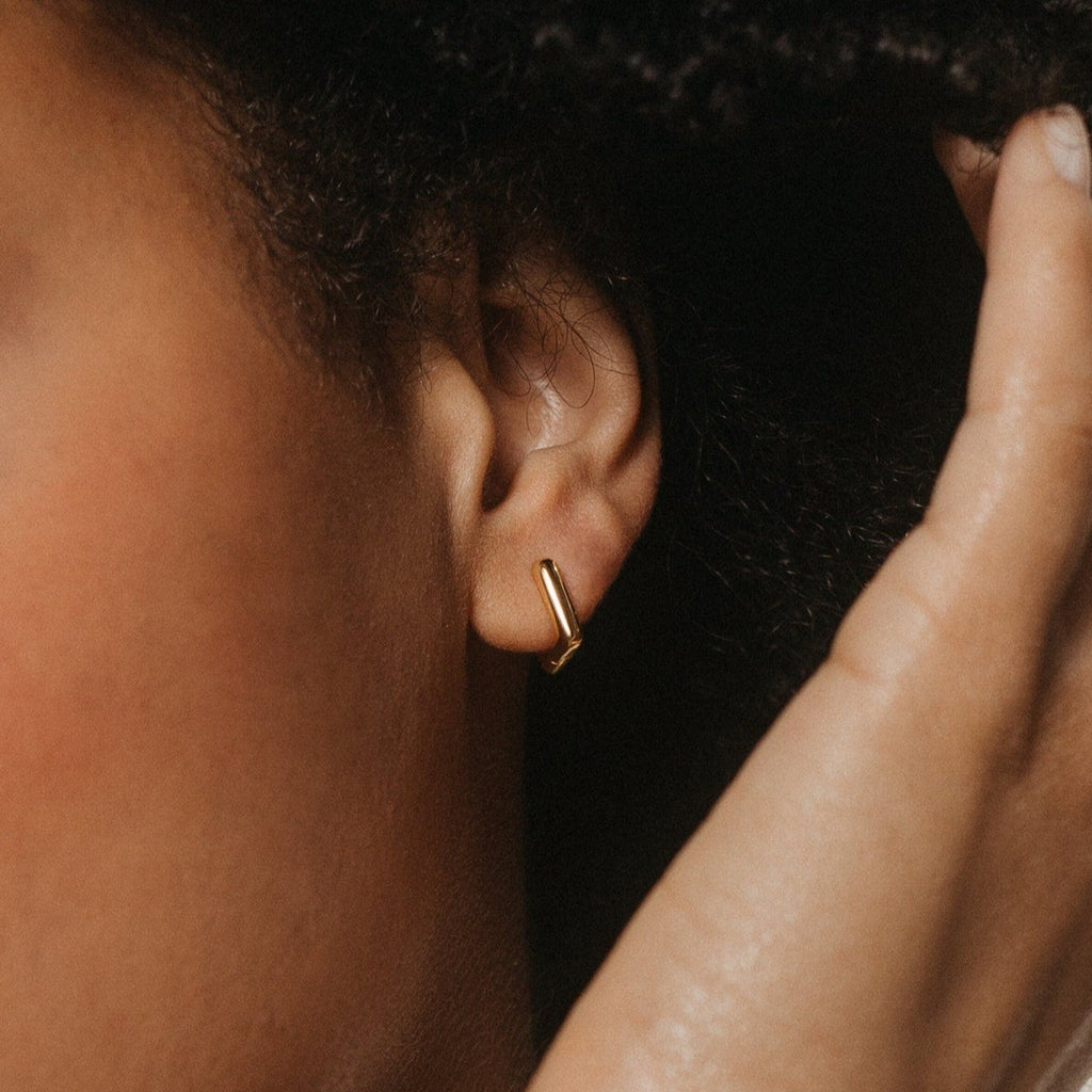 Close-up of a person’s ear wearing Kelsey Link Earrings—a minimal gold accessory—while a hand gently touches their hair.