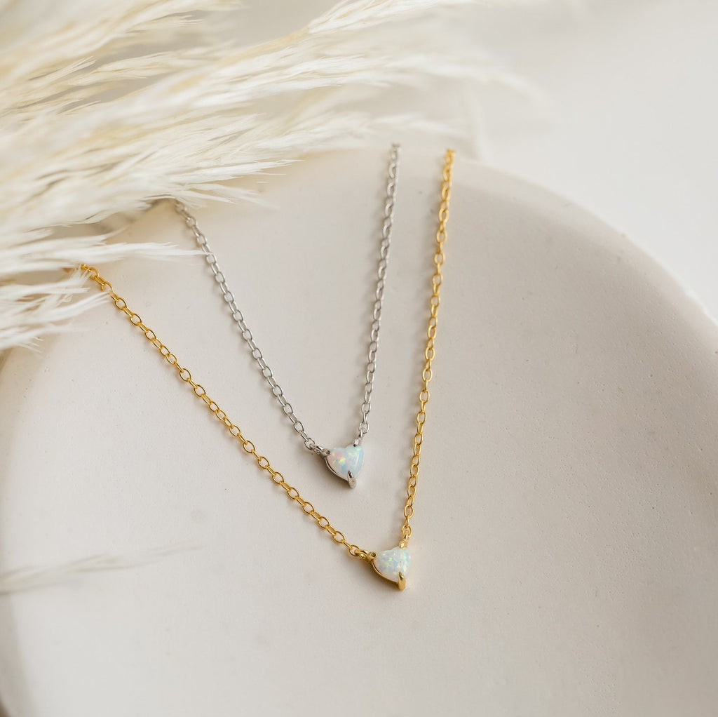 The Madeline Opal Heart Necklace duo features two delicate, dainty necklaces with small opal heart pendants in gold and silver, beautifully displayed on a ceramic dish—perfect for any style.