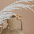 The Elora Baguette Wrap Ring, adorned with clear stones and diamond crystal baguettes, sits elegantly on a beige ceramic vase beside white pampas grass.