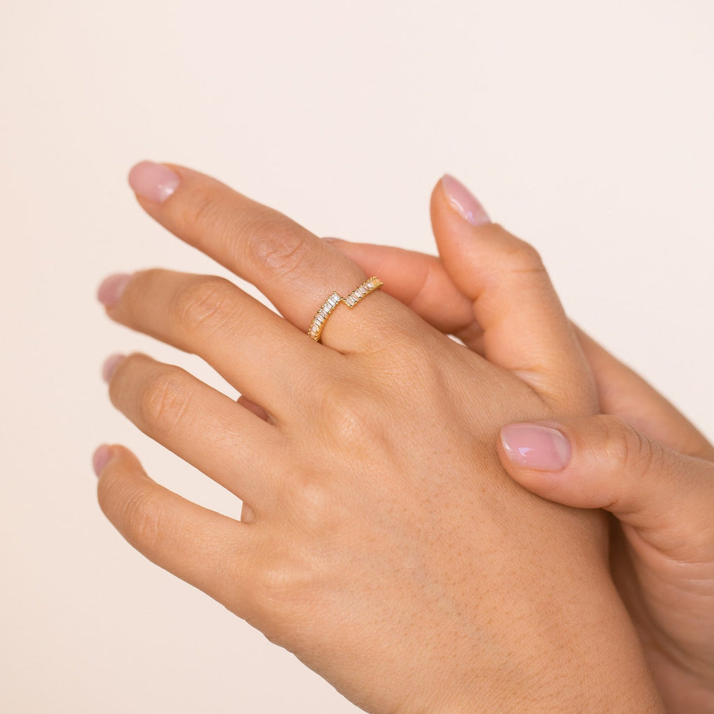A hand wearing the delicate Elora Baguette Wrap Ring, featuring sparkling crystal baguettes, softly touches the other hand's fingers.